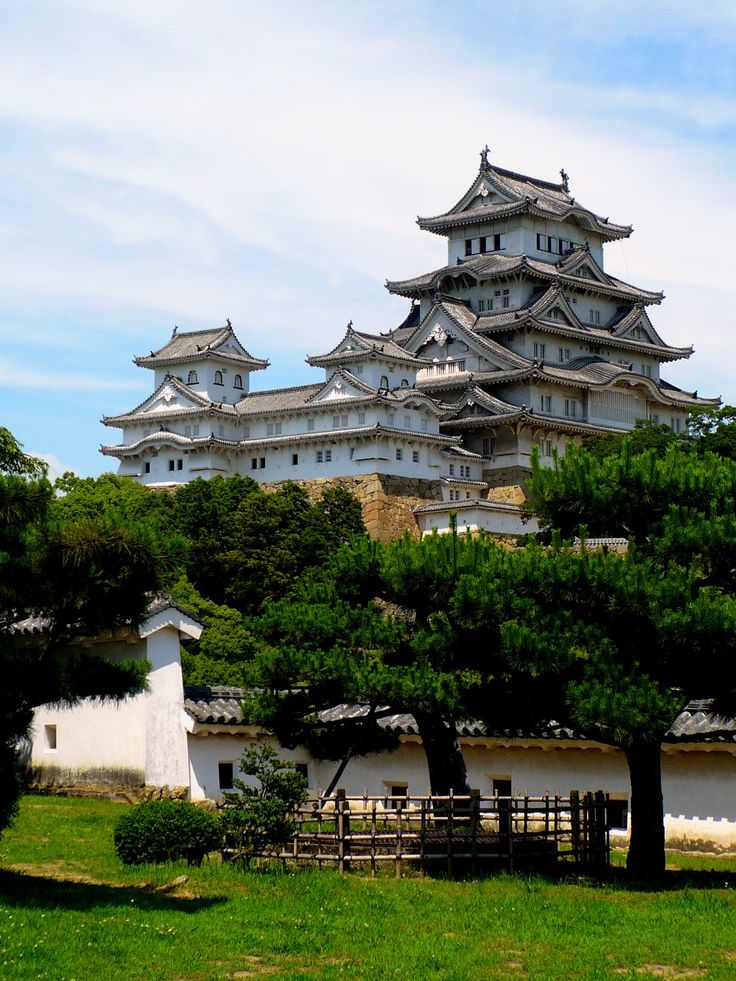 a tall white building sitting on top of a lush green hillside next to trees and grass