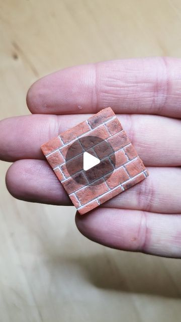 a hand holding a small piece of brick with a video playing button in it's center