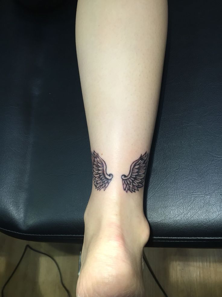 a woman's foot with an angel wing tattoo on her left leg and black leather chair in the background