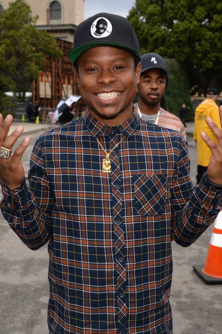 a man in plaid shirt and hat standing next to orange cones with his hands up