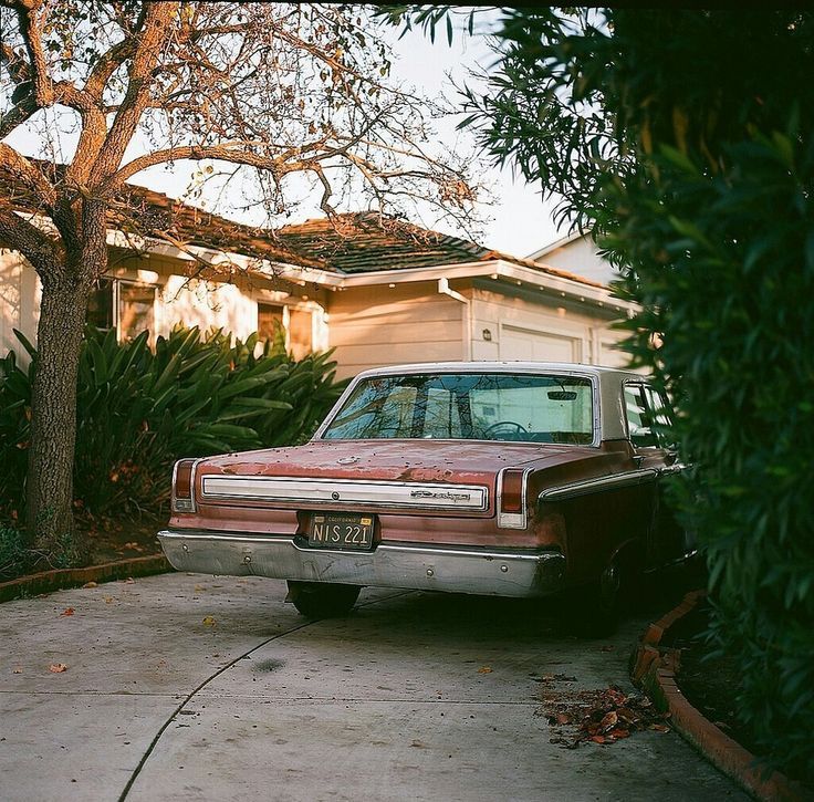 an old car parked in front of a house with trees and bushes around it's perimeter