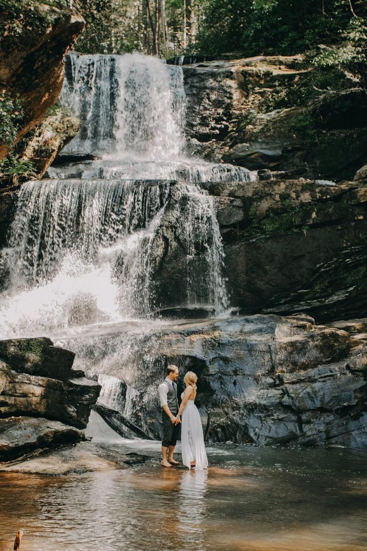 a man and woman standing in front of a waterfall