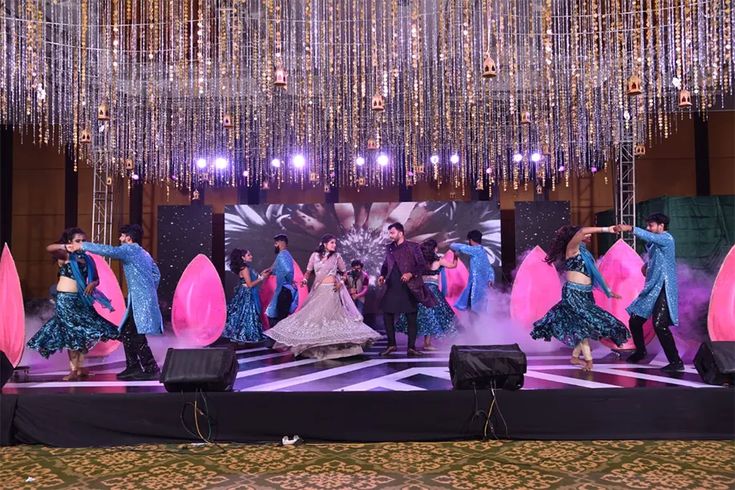 a group of people dancing on stage with chandeliers hanging from the ceiling behind them