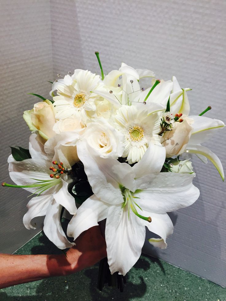 a bouquet of white flowers sitting on top of a green table next to a person's hand