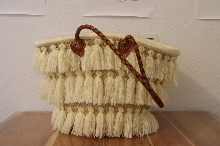 a white purse sitting on top of a wooden table next to a wall with pictures