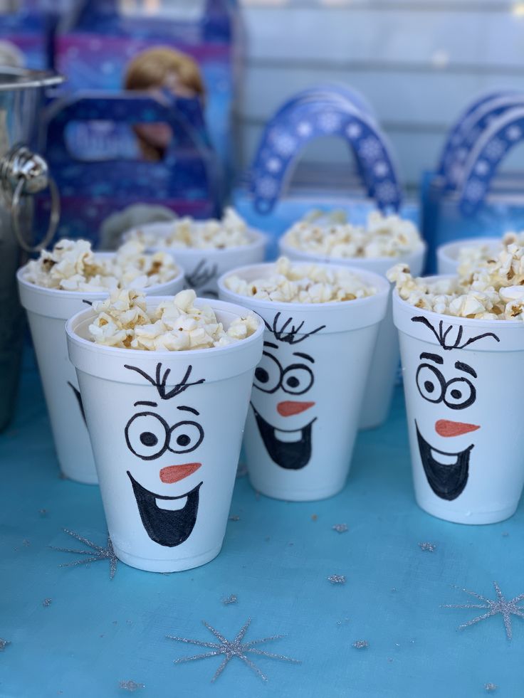 the cups have faces drawn on them and popcorn is in front of some other items