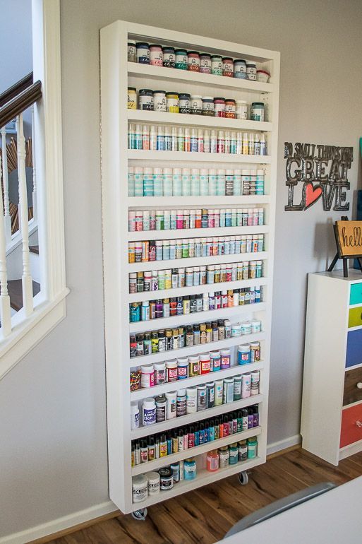 a white shelf filled with lots of different types of paint and other items next to a stair case