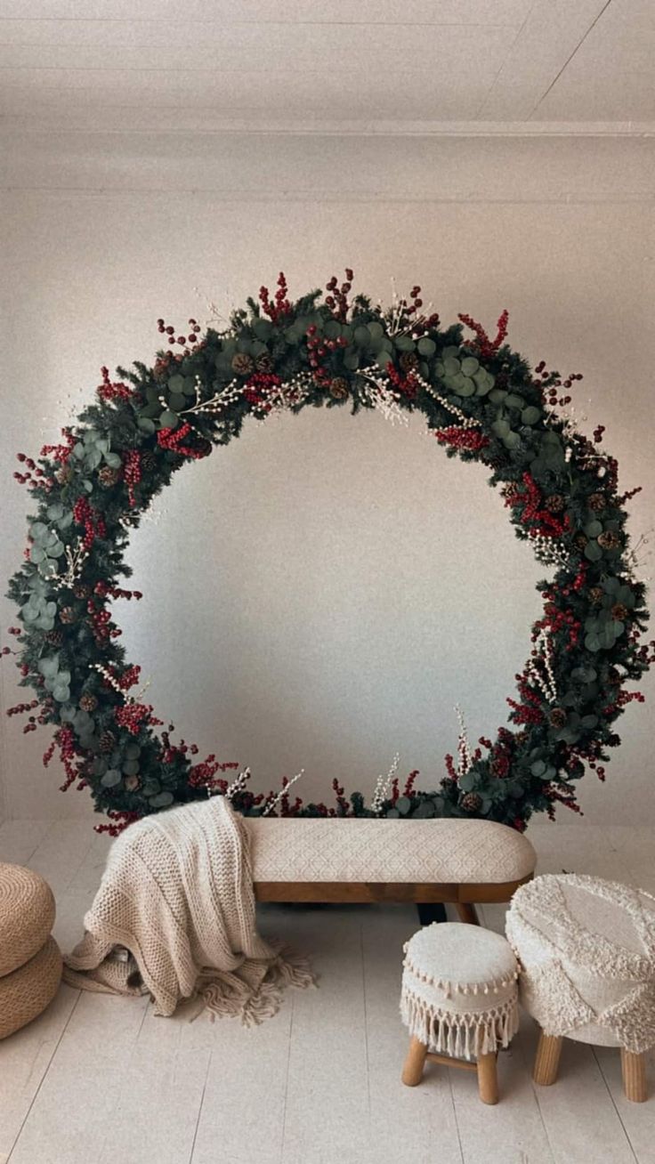 a christmas wreath is hanging on the wall next to two stools and a round mirror