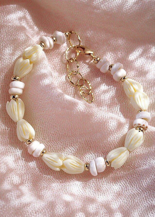 Flanked with natural white puka shells and pikake flowers, this unique shell bracelet evokes visions of Hawaii's white sands and soothing shores. Stack this gold bracelet with other beaded beauties and you'll be ready for your tropical escape.✦ DETAILS ✦✧ Name: Me'e (MAY aye) - Heroine.✧ Adjustable from 6.5"-8".✧ 6-7mm White Puka Shells.✧ Carved Resin Pikake Flowers.✧ 14kt Gold Filled with lobster clasp.✧ All Ke Aloha Jewelry pieces come packaged thoughtfully, beautifully, and ready for gift giv White Shell Beachy Bracelets, White Shell Beachy Bracelet, Beachy White Shell Bracelets, White Beachy Shell Bracelet, White Shell-shaped Beaded Bracelets For Vacation, Handmade White Pearl Bracelet For Vacation, White Beaded Pearl Bracelet For Vacation, White Bohemian Shell Bracelet, White Hand-strung Bracelets For Vacation