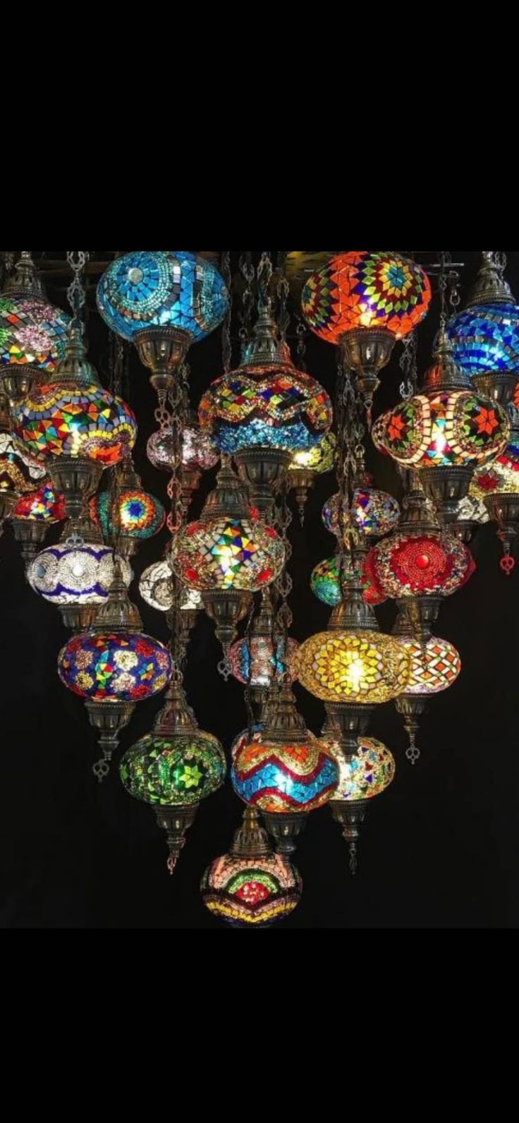 an assortment of colorful glass lamps hanging from the ceiling in a room with black walls