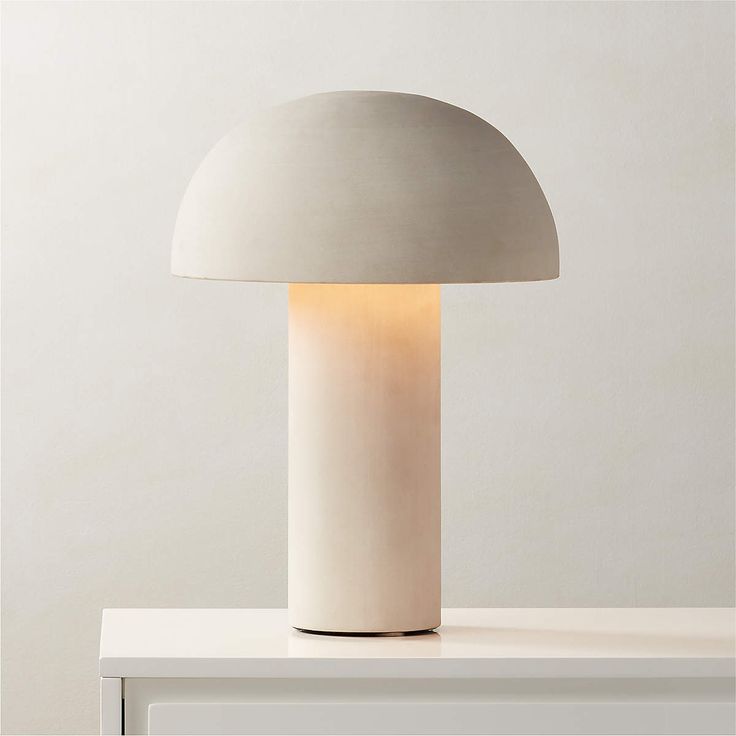 a white lamp sitting on top of a table next to a light gray wall behind it