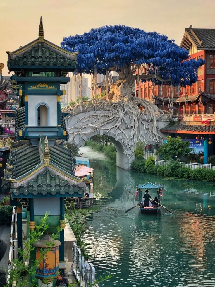 a boat traveling down a river next to tall buildings with trees growing on top of them