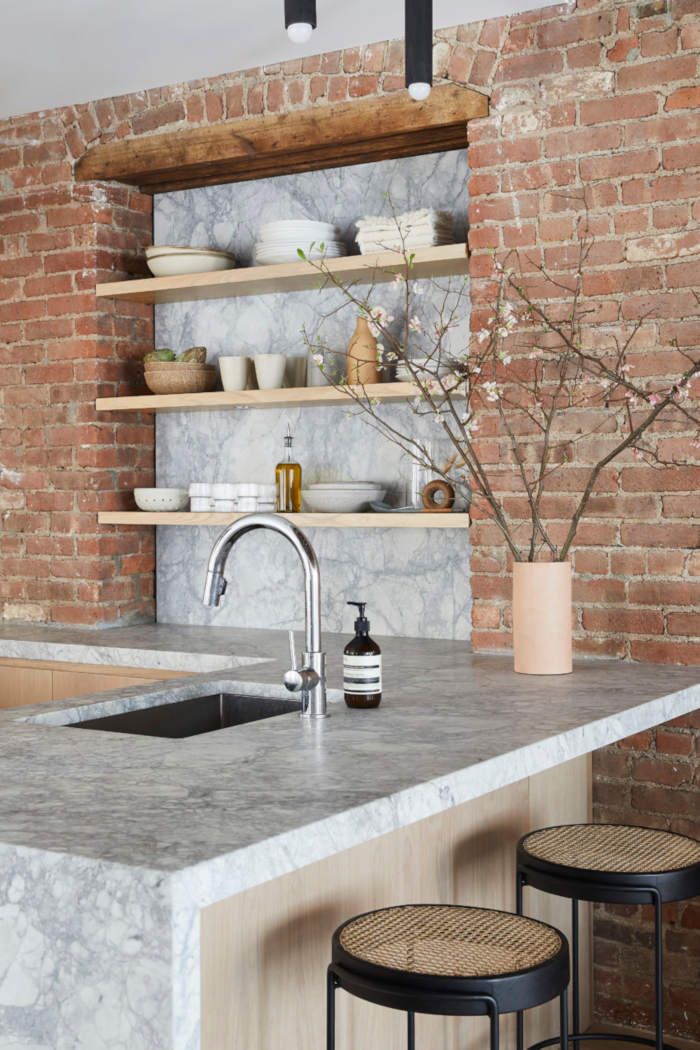 a kitchen with brick walls and marble counter tops, two stools are in front of the sink