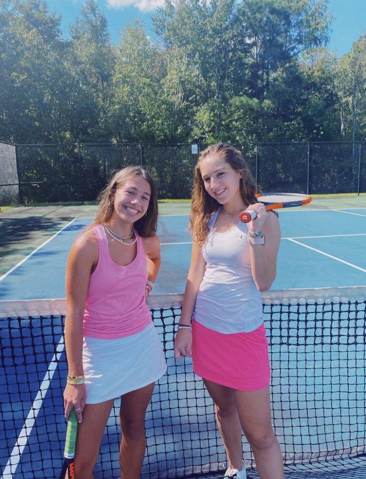 two young women holding tennis racquets on a tennis court