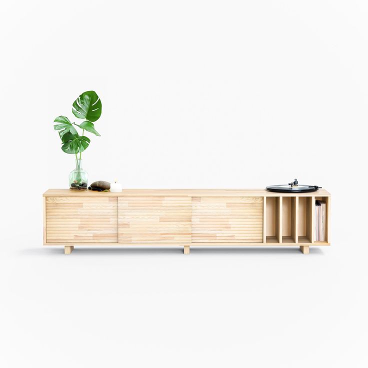 a record player sitting on top of a wooden cabinet next to a plant in a vase