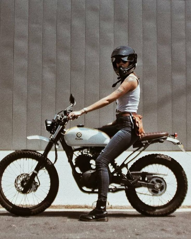 a woman sitting on top of a motorcycle wearing a helmet and holding the handlebars