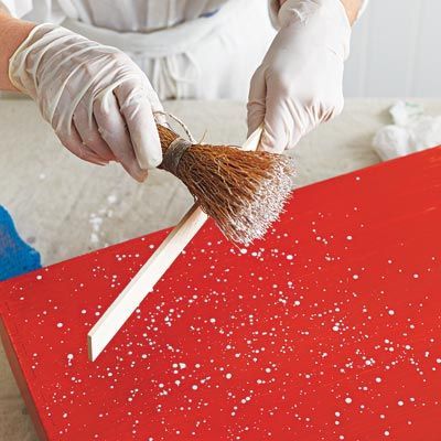 a person in white gloves holding a brush over a red box with snow flakes on it