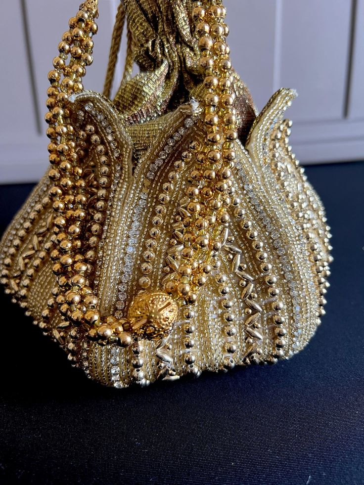 Looking for a stylish and trendy accessory to complete your ethnic ensemble? Look no further than our stunning Gold color potli bag! Handcrafted with care and attention to detail, this elegant bag is the perfect way to add some extra sparkle to your special occasion outfit. Made from high-quality materials, this potli bag features a shimmering gold color that catches the light beautifully. The soft, luxurious texture of the fabric is complemented by intricate embroidery and beadwork, creating a Gold Potli Bag With Latkans For Reception, Traditional Hand Embellished Lehenga For Formal Occasions, Traditional Hand Embellished Formal Lehenga, Elegant Evening Lehenga With Zari Work, Formal Embroidered Gold Lehenga, Formal Gold Embroidered Lehenga, Elegant Festive Lehenga For Festivals, Elegant Lehenga For Festivals, Bohemian Beaded Potli Bag For Wedding