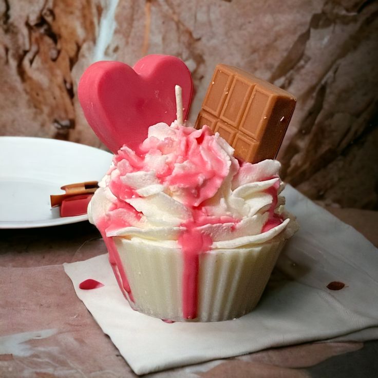 a cupcake with pink frosting and chocolate on top, next to a plate