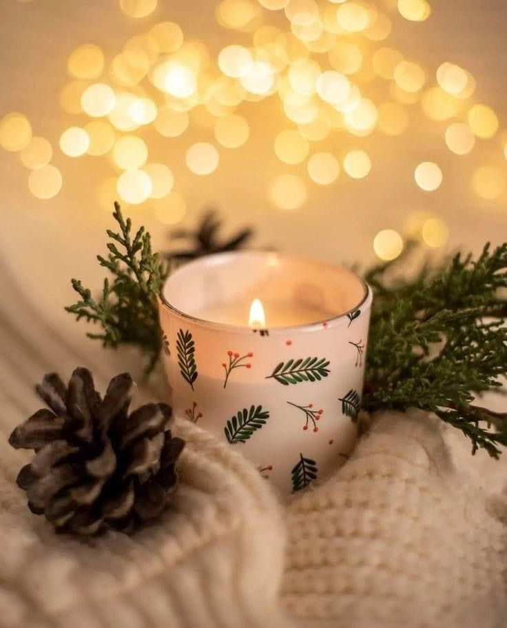 a white candle sitting on top of a table next to a pine cone and sweater