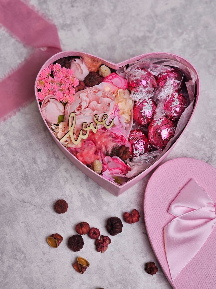 a heart shaped box filled with assorted candy and candies next to a pink hat