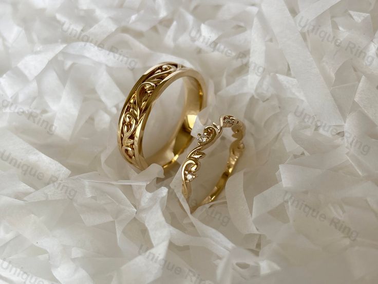 two gold wedding rings sitting on top of white tissue paper with the word love written in it