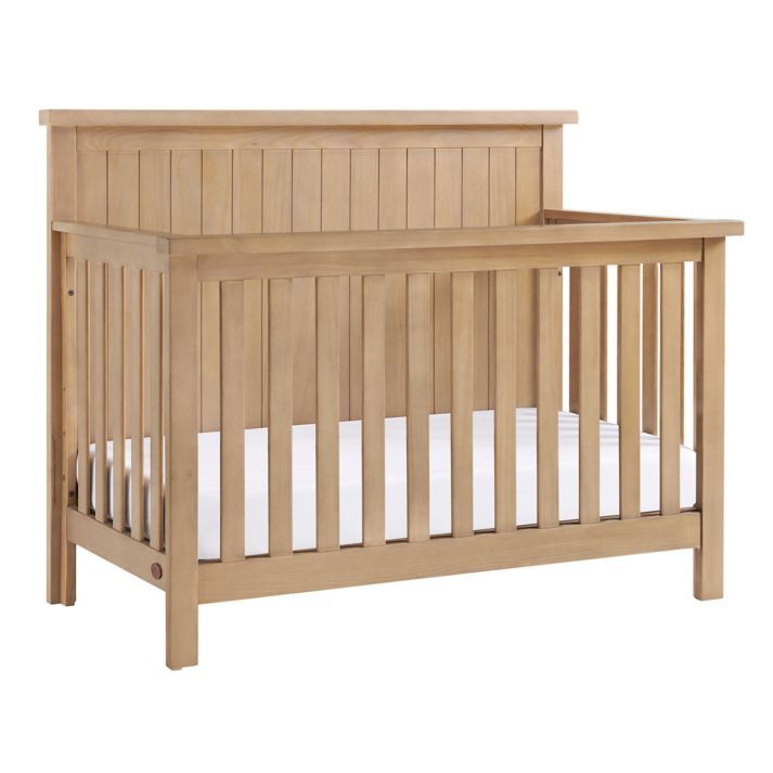 a small wooden crib with white sheets on the bottom and side rails, in front of a white background