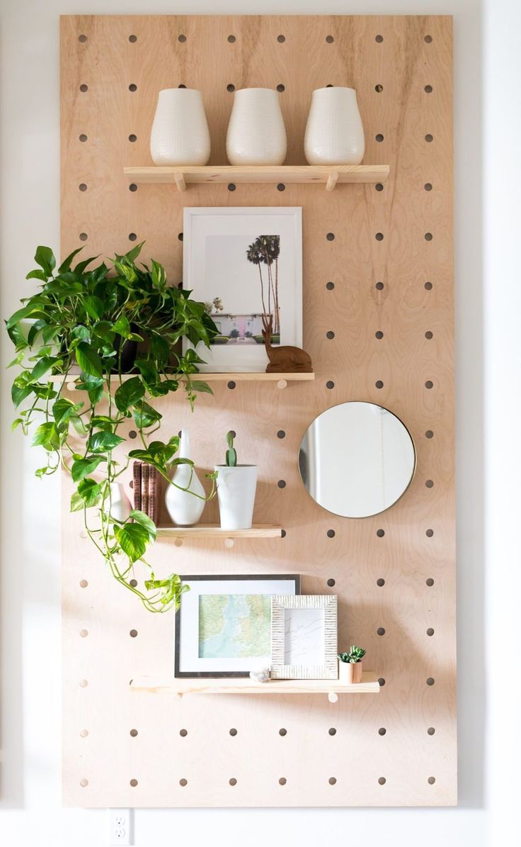 a wooden shelf with potted plants and pictures on it next to a wall mounted mirror