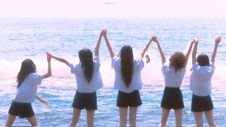 four girls are standing on the beach with their arms in the air and one girl is holding her hands up