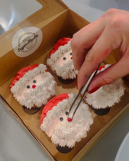 a person cutting into some cupcakes in a box with santa clause decorations on them