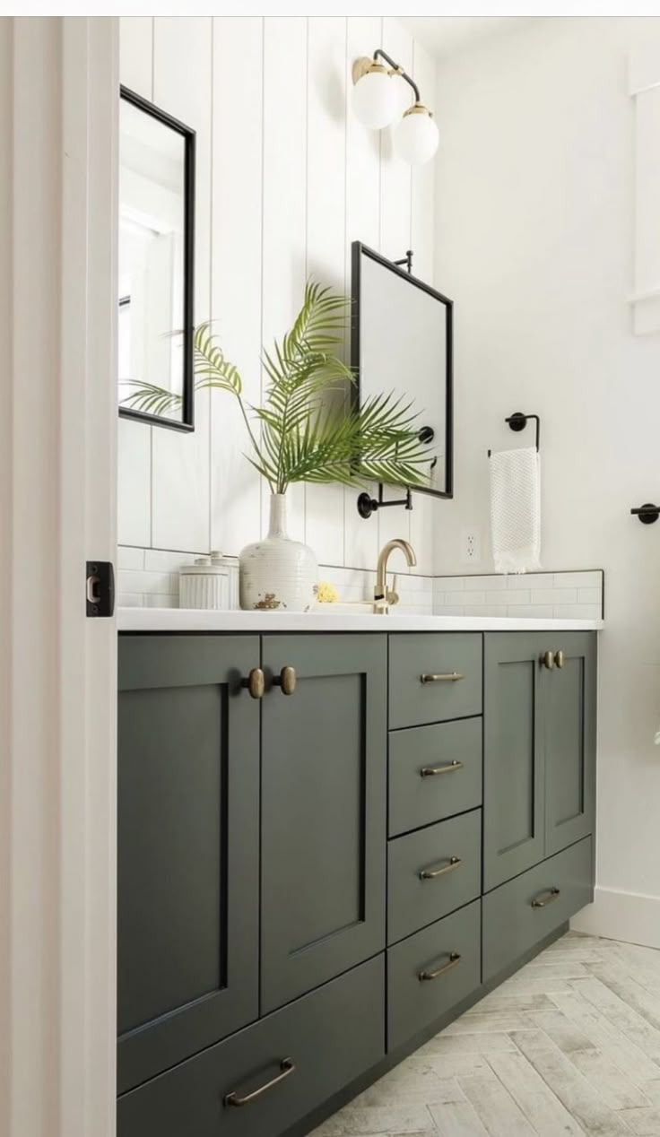 a bathroom with two sinks and mirrors on the wall next to a plant in a vase