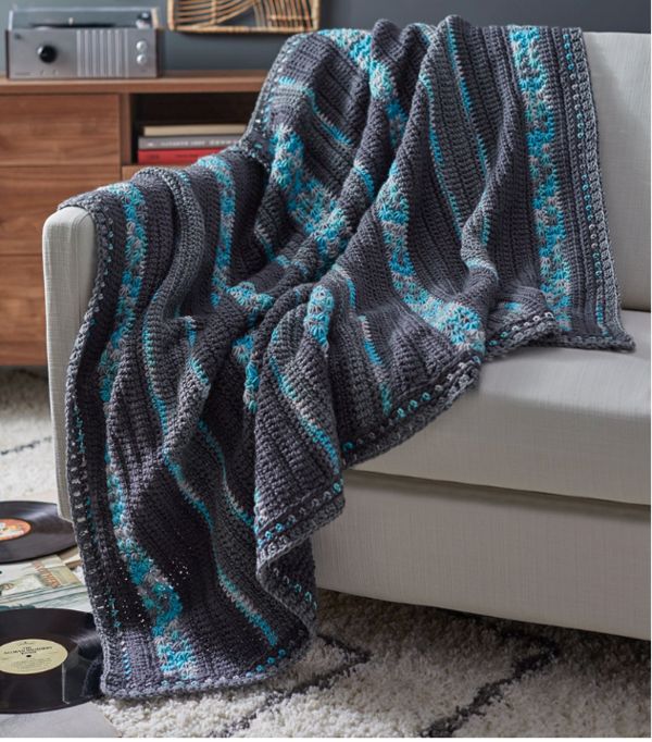 a gray and blue blanket sitting on top of a couch next to a white chair