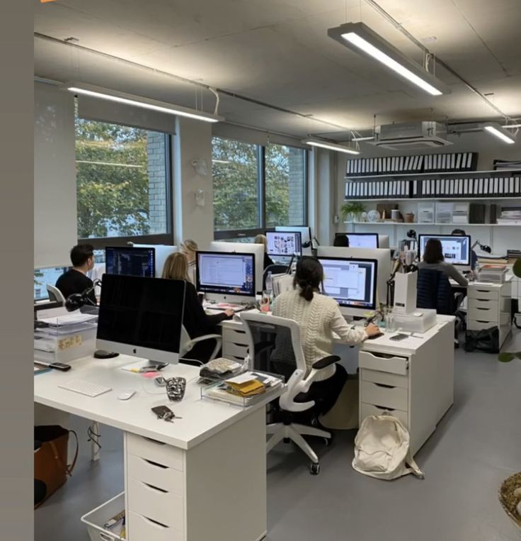 an office filled with lots of computers and people sitting at desks in front of large windows