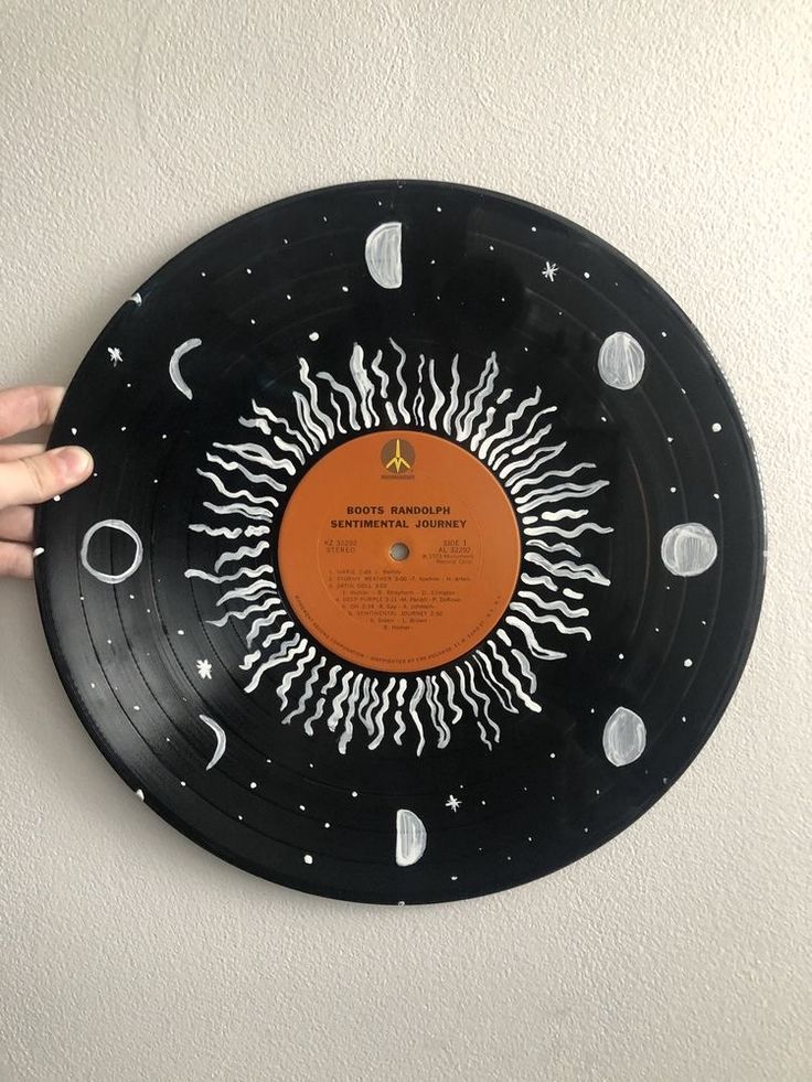 a hand is pointing at an orange and black record on a white wall with stars