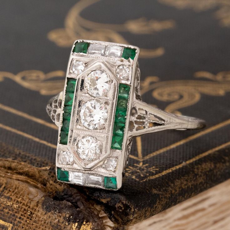 An Art Deco dinner ring studded with Old European cut diamonds, step cuts, and juicy green emeralds! This ring is full of impeccable detail, not to mention she covers up a significant amount of finger real estate! The color combination of diamonds and green emeralds is one that we cannot help but love, especially when set in an original Deco-era beauty. 18kt white gold Size 7.5 & fully resizable Diamond Measures: 5.67 x 5.67 x 3.94 mm Diamonds are estimated to be G/I colors & VVS/VS clarities. G Green Diamond Ring With Single Cut Emerald Shape, Green Emerald Cut Diamond Ring With Single Cut Diamonds, Emerald Cut Green Diamond Ring With Multi-stone, Emerald Cut Green Multi-stone Diamond Ring, Green Emerald Cut Multi-stone Diamond Ring, Art Deco Green Ring, Gia Certified, Art Deco Green Ring Gia Certified, Exquisite Green Emerald Ring With Diamond Accents, Platinum Emerald Ring With Diamond Accents