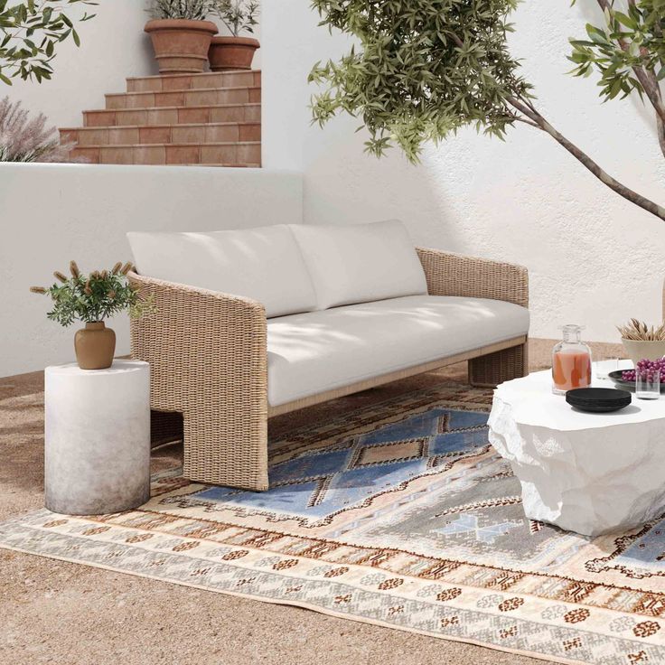 a white couch sitting on top of a rug next to a table and potted plants