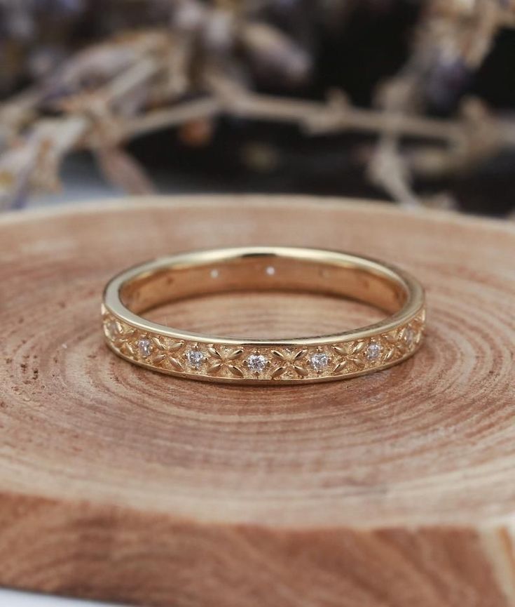 a gold wedding band with small diamonds on top of a piece of wood, next to some dried flowers