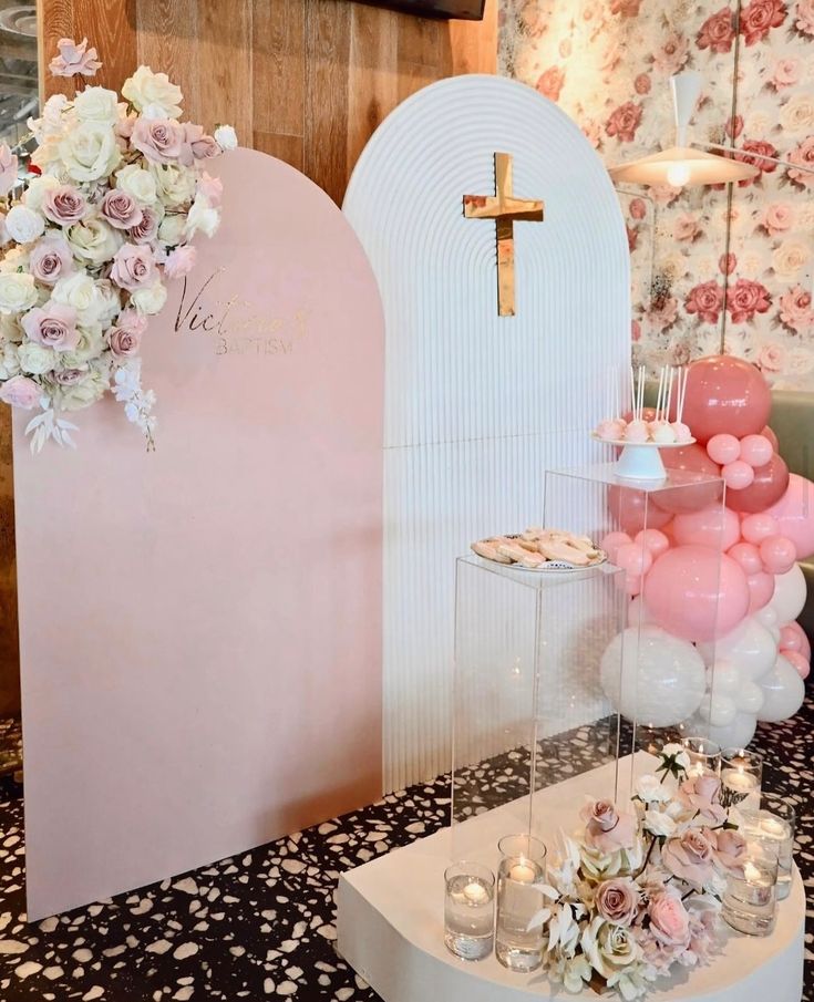 a table topped with lots of pink and white balloons next to a wall covered in flowers