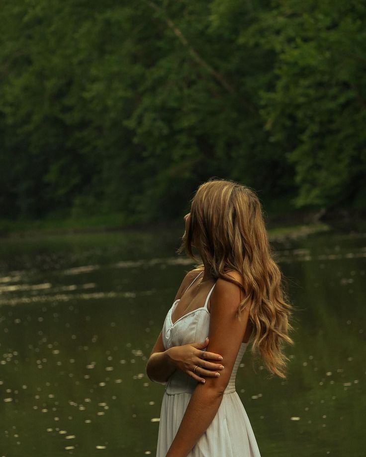 a woman in a white dress standing next to a lake