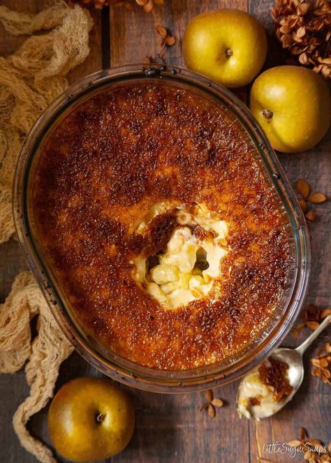 an apple pie in a glass dish on a wooden table with apples and cinnamons around it