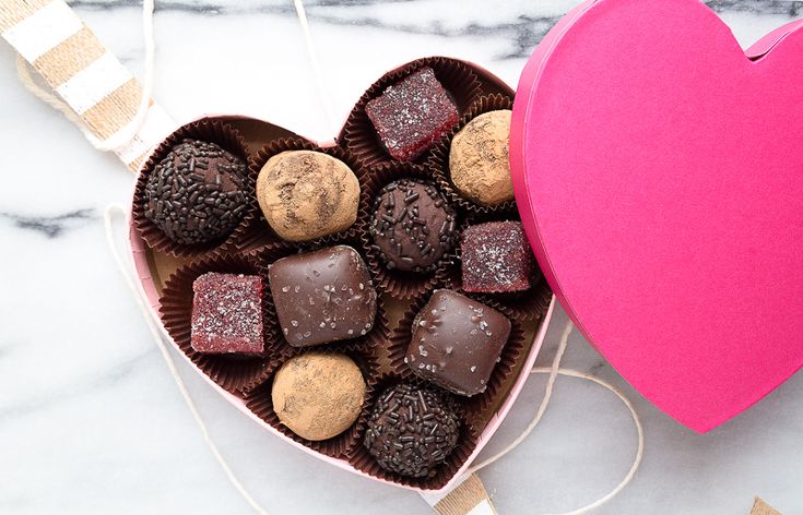 a heart shaped box filled with assorted chocolates next to a pink paper heart