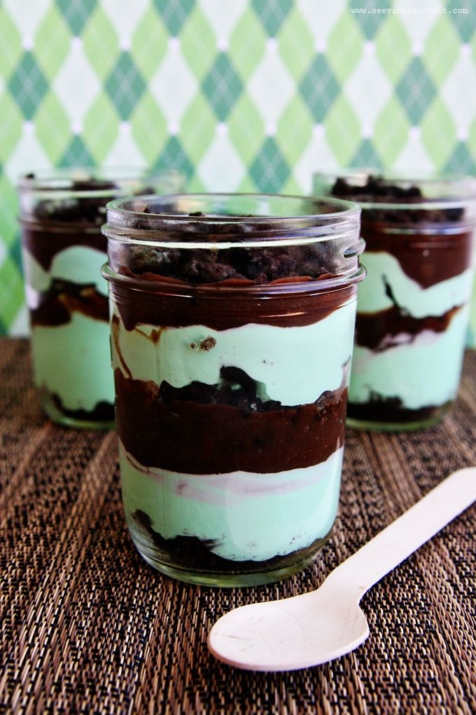 three desserts with chocolate and mint filling in glass jars next to a spoon on a woven tablecloth