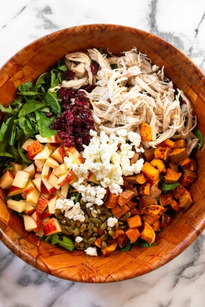 a wooden bowl filled with different types of food on top of a marble countertop