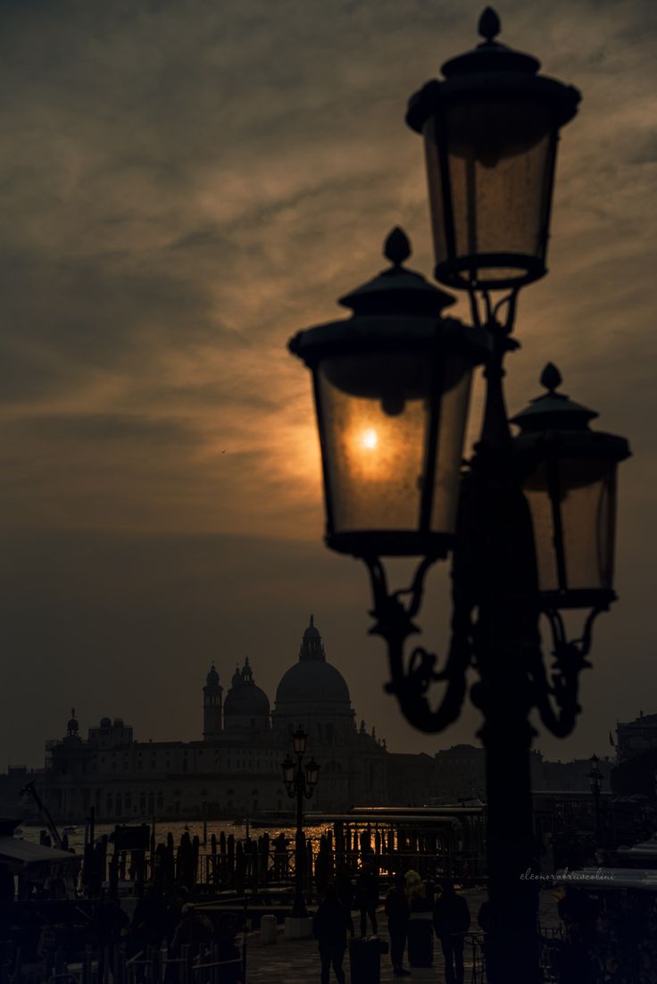 the sun is setting behind two street lamps