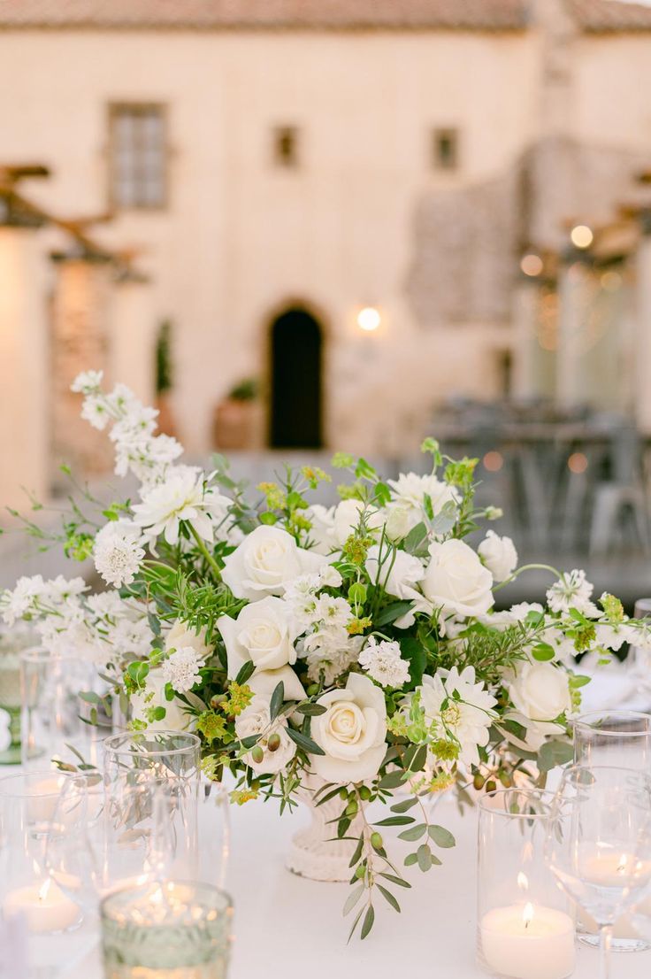 white flowers and greenery are arranged in glass vases on a table with candles