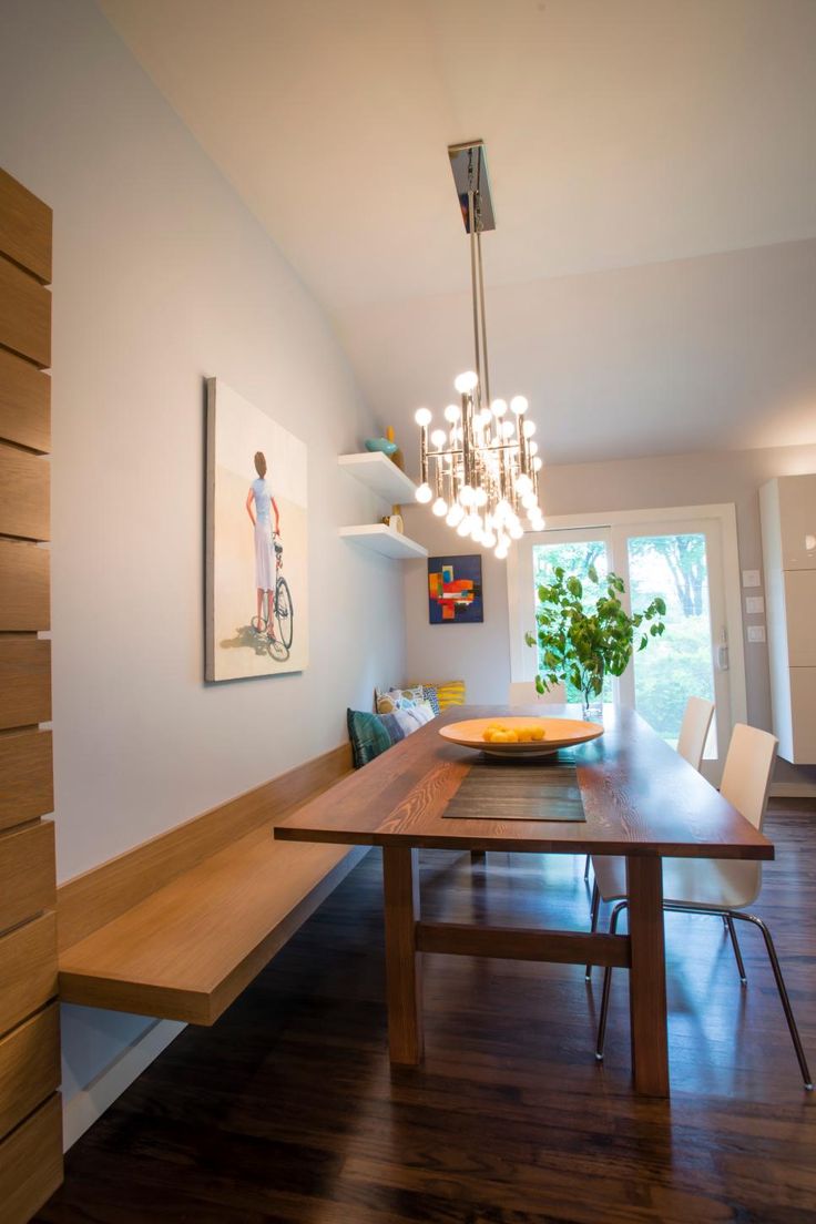 a dining room with a wooden table surrounded by white chairs and hanging chandelier