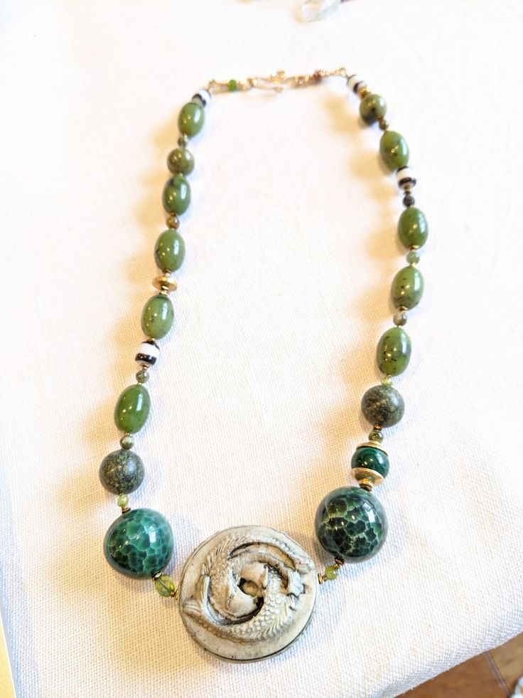 Amazing two fish center piece inspired this Agate , jade and gold necklace. Older striped Czech beads, peridot and malachite beads meant for "HARMONY and ABUNDANCE" Jade Amulet Necklace With Natural Stones, Green Agate Jewelry With Natural Stones, Spiritual Green Agate Jewelry, Green Agate Jewelry For Healing, Green Jade Amulet Necklace, Green Amulet Jewelry With Natural Stones, Green Malachite Gemstone Bead Jewelry, Green Aventurine Amulet Jewelry, Green Agate Pendant Necklace