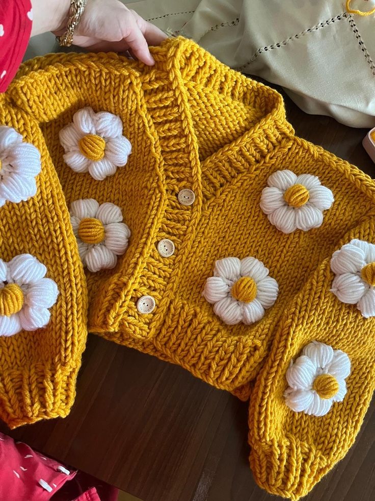 two yellow sweaters with white flowers on them sitting next to a woman's purse