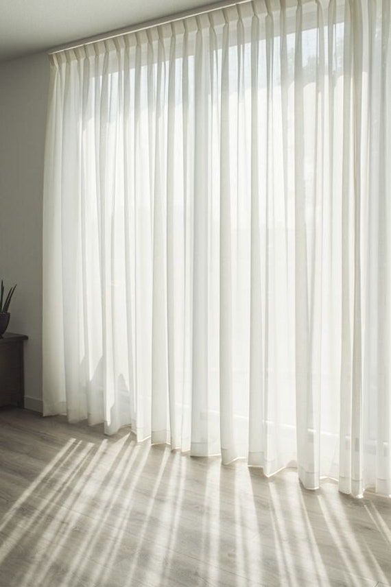 the sun is shining through the curtains in this room with wood flooring and large windows