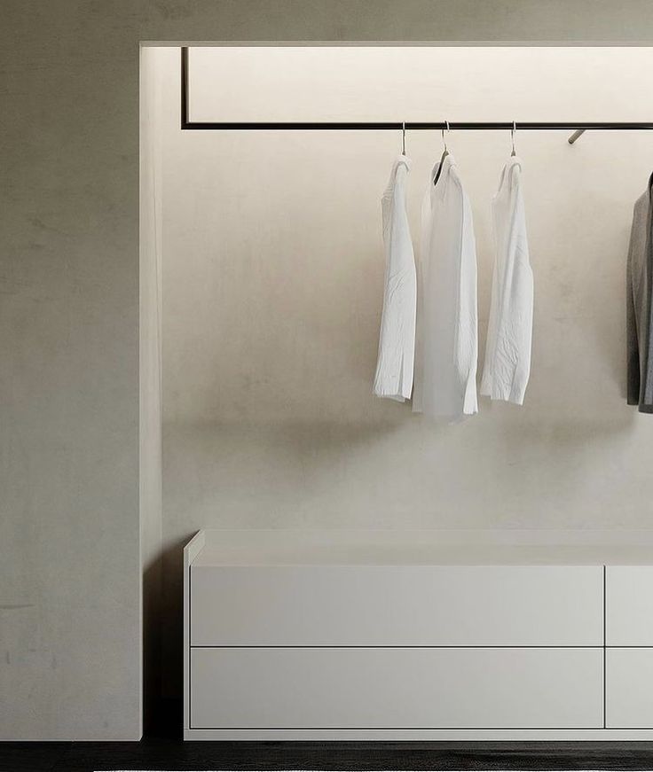 three white shirts hanging on the clothes rail in front of a gray wall and floor